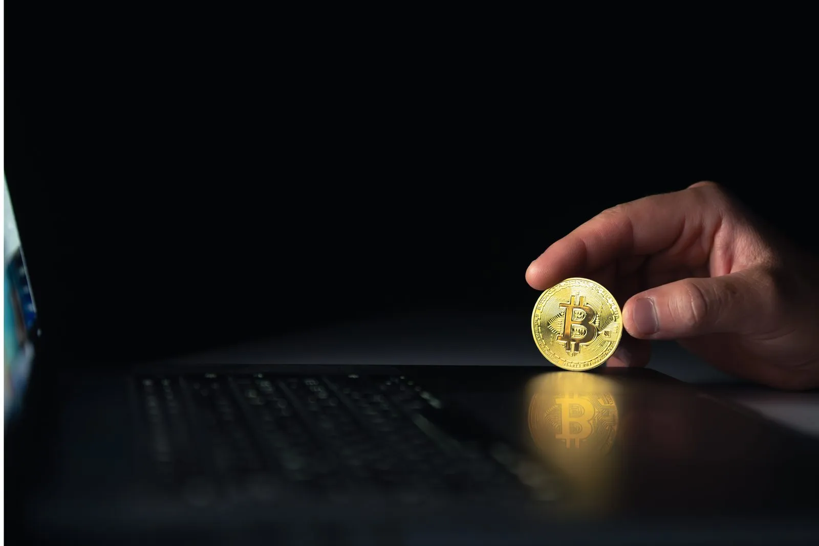 Moneta bitcoin obok laptopa na ciemnym tle - MiCA a obowiązki AML dostawców kryptoaktywów